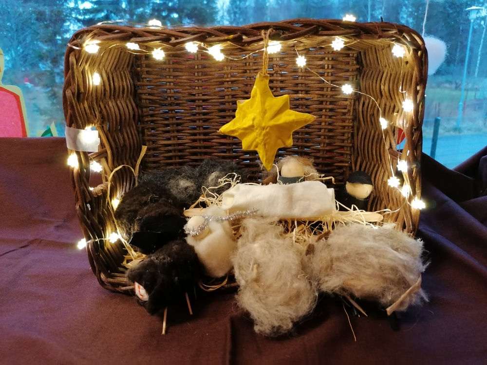 Jouluseimi, jossa on Jeesus-lapsi perheineen ja enkeli sekä eläimiä ympärillä. Taustalla on iso tähti ja pi...